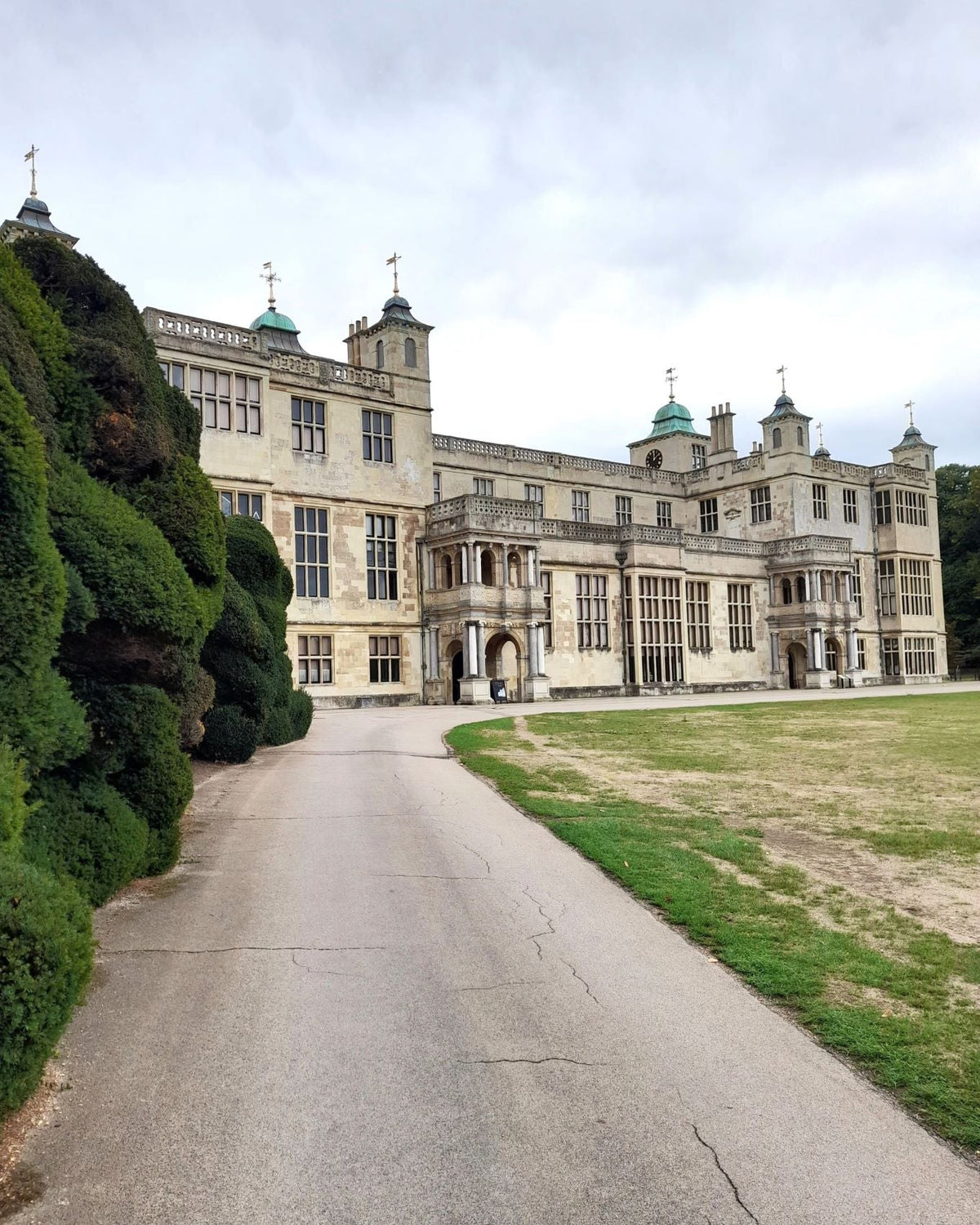 Front view of Audley End House, Essex, showing its magnificent historic stone façade and a wide driveway leading to the main entrance.