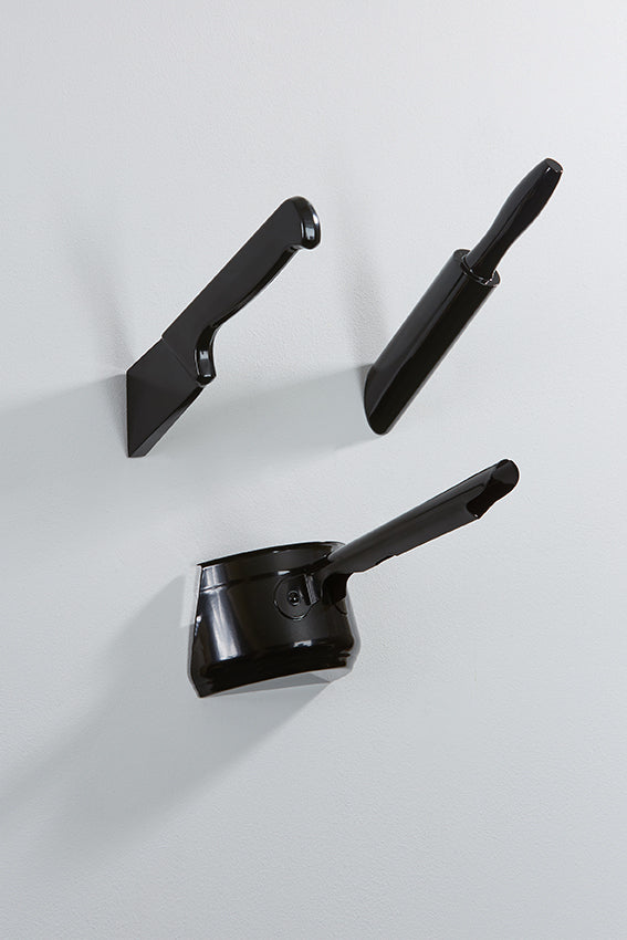A black set of wall hooks in the shape of a saucepan, knife and rolling pin that look like they are embedded in the wall.