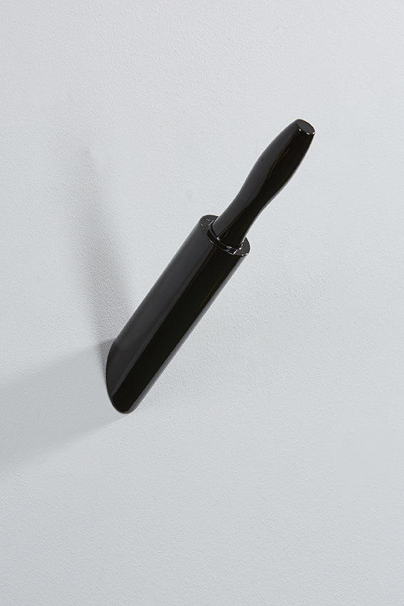 A wall hook shaped like a rolling pin that appears embedded in the wall, black in colour